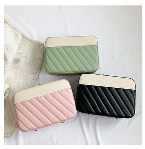 Three quilted makeup bags in pink, green, and black with cream trim and metal feet detail