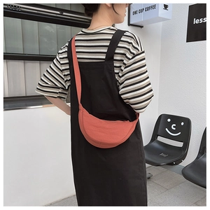 Detail view of coral nylon dumpling bag worn by model, showing texture and curved shape