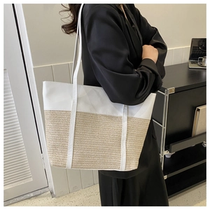 Detail of a large woven tote bag with white leather contrast and dual shoulder straps