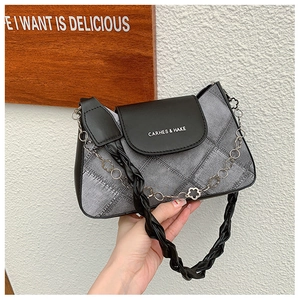 Close-up of grey denim shoulder bag featuring black leather flap and silver chain link