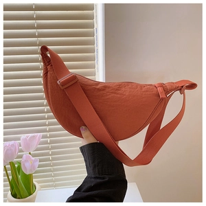 Detail of orange nylon crescent bag showing crinkled texture and adjustable strap
