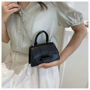 Detail of black crossbody bag with silver chain strap and metal buckle shown on a model