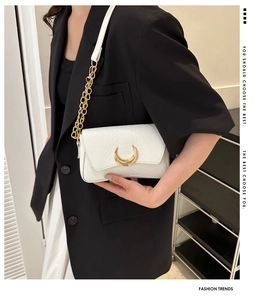 Close-up of white croc-embossed leather bag featuring a gold crescent metal buckle