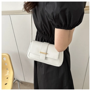 Détail du sac à bandoulière en cuir blanc avec barre dorée porté par un mannequin