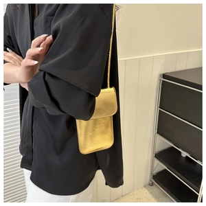 Mini sac de téléphone doré brillant porté en bandoulière dans un cadre de vie élégant