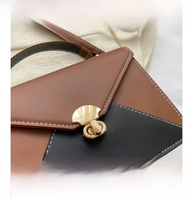 Close-up of color-block leather handbag with white stitching and gold turn-lock buckle