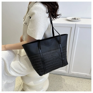 Detail of a large black tote bag featuring smooth leather and woven textured patchwork