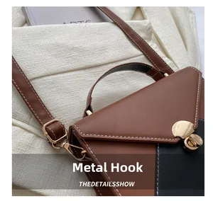Close-up of golden metal hooks and white stitching on the bicolor leather shoulder bag