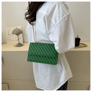 Dettaglio borsa baguette in ecopelle trapuntata verde con catena dorata su una modella