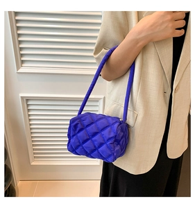 Detailed view of a bright blue quilted nylon puffy mini handbag styled with a beige blazer
