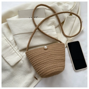 Close-up of woven bucket bag with pearl closure on a stylish textured white fabric background