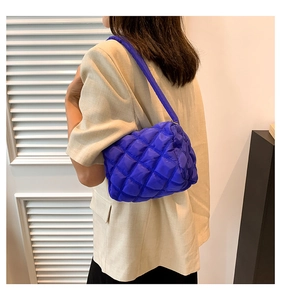 Detailed side view of the bright blue quilted puffer shoulder bag worn by a model