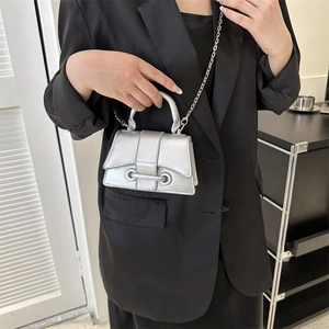 Metallic silver trapezoid handbag with top handle and chain strap worn by a model
