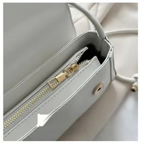 Détail de la fermeture éclair dorée et accessoires sur le sac à main blanc cassé
