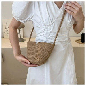 Detail of hand-woven straw crossbody bag with white pearl clasp on a white dress model