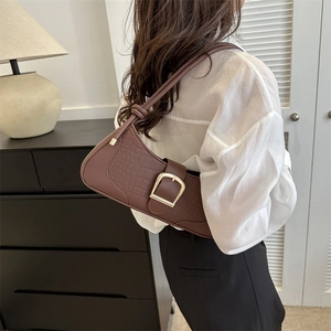 Sac sous le bras marron à motif crocodile avec boucle dorée porté par un mannequin