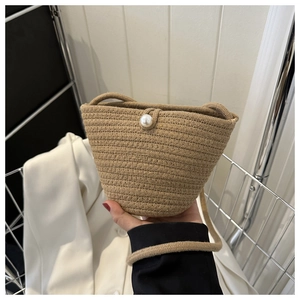 Detail of straw woven bucket bag with large pearl clasp and khaki woven texture