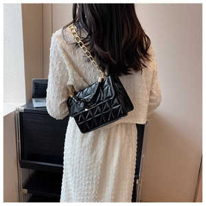 Close-up of black quilted shoulder bag with gold chain strap on a white dress