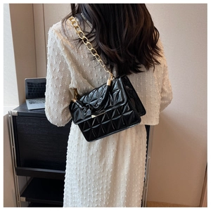 Detail of black quilted patent leather handbag with a chunky gold chain strap on model