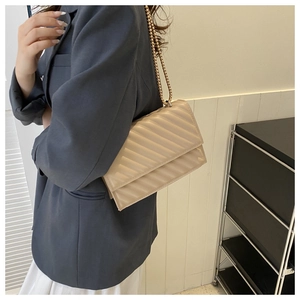 Dettaglio borsa trapuntata beige con catena dorata su modella con un completo elegante