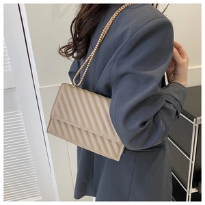 Dettaglio della borsa a tracolla trapuntata beige con catena dorata indossata da una modella
