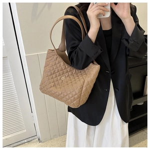 Close-up of brown quilted leather tote bag featuring a gold clover logo and fine stitching