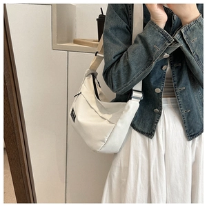 Detailed close-up of a cream canvas half-moon crossbody bag styled with a denim jacket