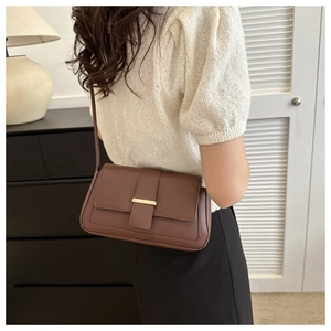 Détail d'un sac bandoulière en cuir mat marron foncé avec garniture dorée porté par un modèle