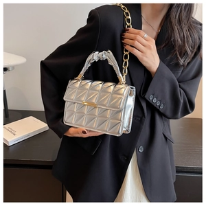 Silver quilted crossbody bag with gold chain strap held by a model in a black suit