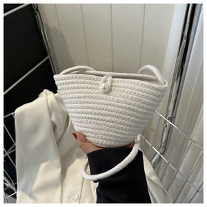 Detail of white hand-woven bucket bag featuring a decorative pearl clasp and spiral texture