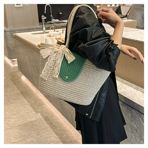 Close-up of beige woven straw tote bag with green flap and white lace bow detail