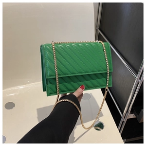 Dettaglio borsa quadrata verde trapuntata con tracolla a catena dorata tenuta in mano