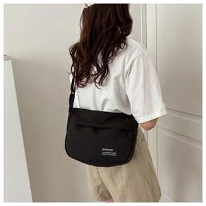 Back view of model wearing a black oxford cloth messenger bag with adjustable strap