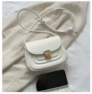 Size comparison of a white minimalist saddle bag next to a smartphone on a beige suit