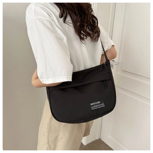 Detail view of a black oxford fabric crossbody bag with a white woven logo patch