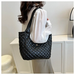 Detail of black quilted puffer tote bag with gold floral emblem worn by model