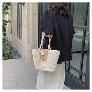 Detail of white woven tote bag featuring a khaki flap and cream lace ribbon bow