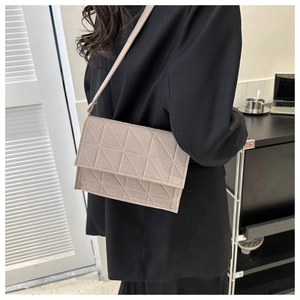 Détail du sac bandoulière en feutre beige à motif géométrique porté avec un blazer noir