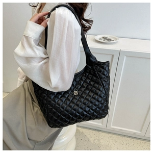 Detail shot of a black quilted tote bag with large diamond patterns and gold flower logo