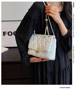 Detail of white quilted crossbody bag featuring triangular stitching and gold metal lock