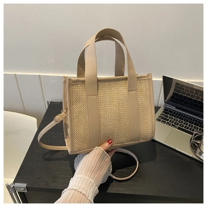 Dettaglio della borsa tote in paglia intrecciata con manici in ecopelle su scrivania