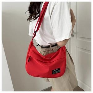 Detail of red oxford sports crossbody bag featuring black logo patch and adjustable strap