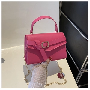 Macro detail of magenta leather handbag with gold chain strap and decorative buckle