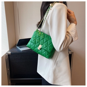 Detail of green quilted leather crossbody bag with gold chain strap on shoulder
