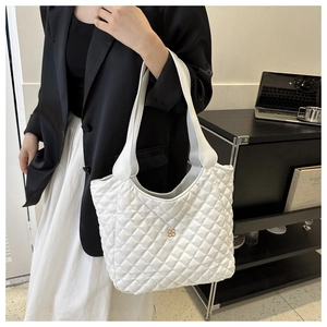 Detailed close-up of white quilted tote bag with golden four-leaf clover logo and wide strap