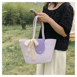 Detail of purple woven tote bag with white lace bow held by model in outdoor park