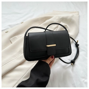 Détail du sac bandoulière en cuir noir minimaliste avec boucle dorée et bandoulière nouée