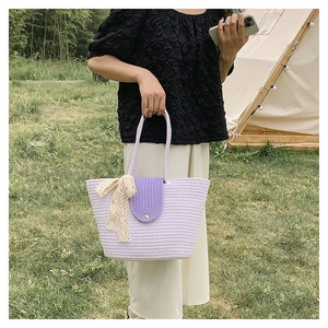 Detail of light purple woven tote bag featuring a deep purple flap and lace bow charm