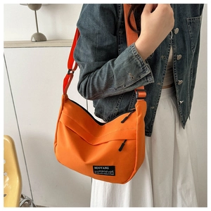 Close-up of vibrant orange nylon crescent bag featuring a black NUOYANG city-silhouette label