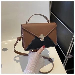 Close-up of color-block envelope bag featuring a gold circular twist lock and handle